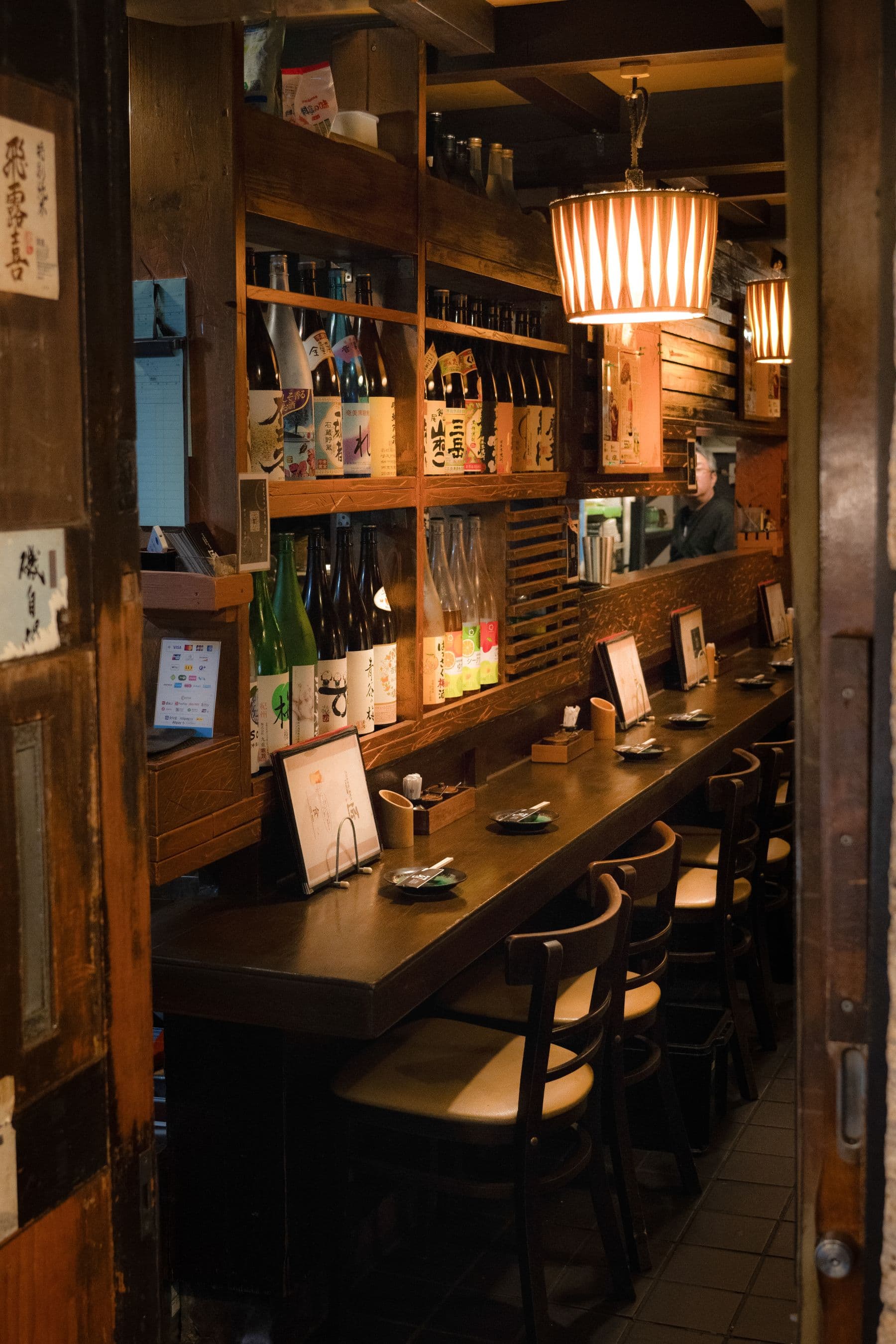 酒瓶の棚とカウンター席が並ぶ、居酒屋の店内